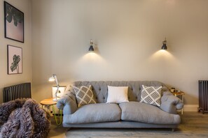 A cozy living room with a grey sofa, two wall-mounted lamps, a small side table, and a furry rug. - Emley Woodhouse - Seven Bedroom Villa, Sleeps 17 (Emley)