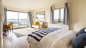 A hotel room with a large bed, a desk, a chair, and a view of the sea through the balcony. - Snow Goose - Five Bedroom Villa, Sleeps 9 (Nutbourne)
