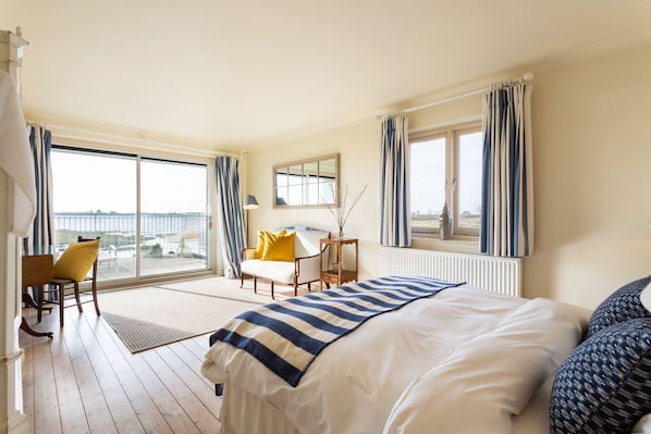 A hotel room with a large bed, a desk, a chair, and a view of the sea through the balcony.