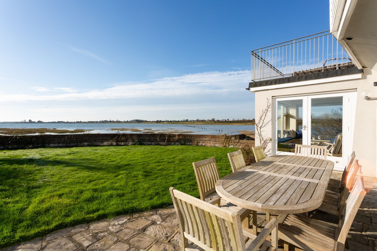 Une terrasse avec une table et des chaises, une pelouse verdoyante et une vue sur la mer.