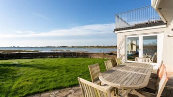 Une terrasse avec une table et des chaises, une pelouse verdoyante et une vue sur la mer.