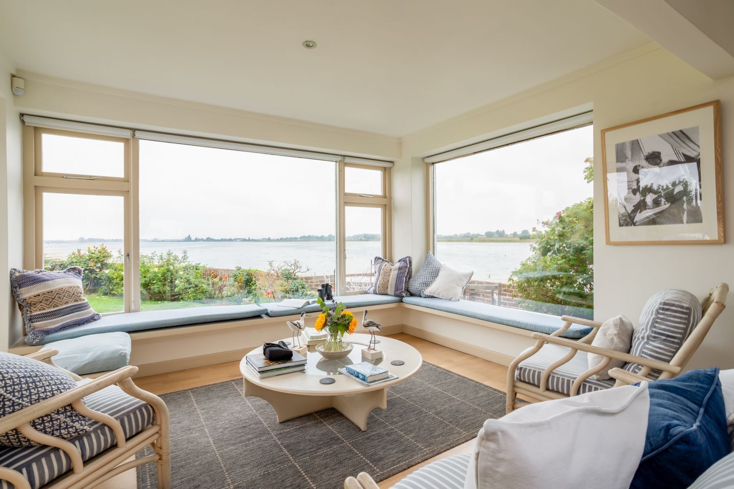 A room with large windows, a round coffee table, and seating with cushions.