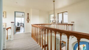 A spacious hallway with a wooden staircase, a chandelier, and a view into another room. - Snow Goose - Five Bedroom Villa, Sleeps 9 (Nutbourne)