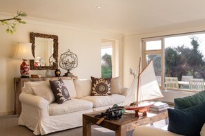 Un salon chaleureux avec un canapé blanc, des coussins décoratifs, une table basse en bois sur laquelle est posé un modèle de voilier, une lampe et un miroir au mur.