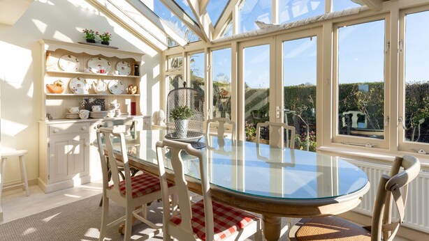 A conservatory with a glass table and chairs, surrounded by shelves with dishes and a view of the garden. - Snow Goose - Five Bedroom Villa, Sleeps 9 (Nutbourne)
