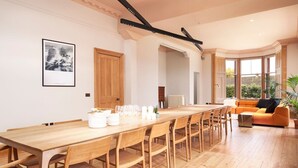 A spacious dining area with a long wooden table and chairs, a modern orange sofa, and a framed picture on the wall.