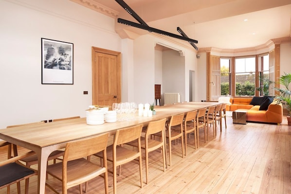 A spacious dining area with a long wooden table and chairs, a modern orange sofa, and a framed picture on the wall. - Hilltop Manor - Nine Bedroom Villa, Sleeps 18 (Aberfeldy)
