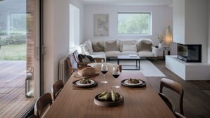 Un comedor con una mesa de madera dispuesta para dos personas, dos platos de comida y dos copas de vino tinto.