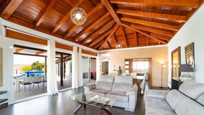 A spacious living area with a high wooden ceiling, a glass coffee table, and a sofa. - Villa Princesa - Four Bedroom Villa, Sleeps 8 (Puerto Calero)
