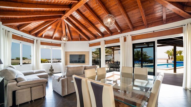A spacious living area with a high wooden ceiling, a glass dining table, and a view of a swimming pool. - Villa Princesa - Four Bedroom Villa, Sleeps 8 (Puerto Calero)