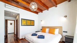 A hotel room with a large bed, wooden flooring, a ceiling with exposed beams, a wall-mounted air conditioner, and a decorative light fixture. - Villa Princesa - Four Bedroom Villa, Sleeps 8 (Puerto Calero)