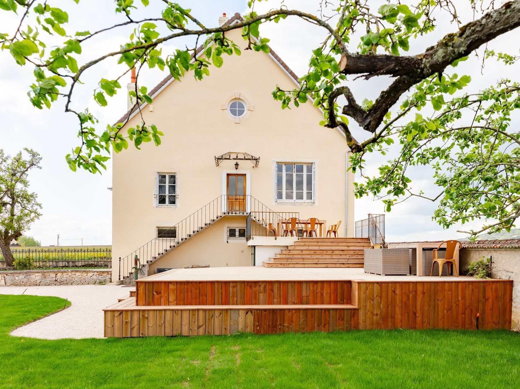 A two-story house with a wooden deck, a staircase, and a small outdoor seating area.