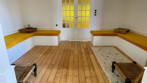 A room with wooden flooring, a white door with a yellow glass panel, and two wicker chairs. - Maison des Grands Crus (Puligny-Montrachet)