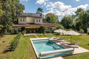 Una casa grande con piscina, mobiliario exterior y jardín.
