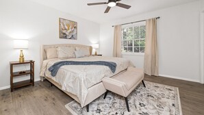 Un dormitorio con cama, lámparas de noche, ventilador de techo, ventana con cortinas y alfombra.