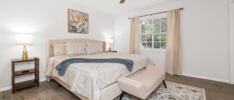 A bedroom with a bed, bedside lamps, a ceiling fan, a window with curtains, and a rug.