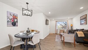 Una sala de estar moderna con zona de comedor, que incluye una mesa redonda con sillas, un sofá y un televisor montado en la pared.