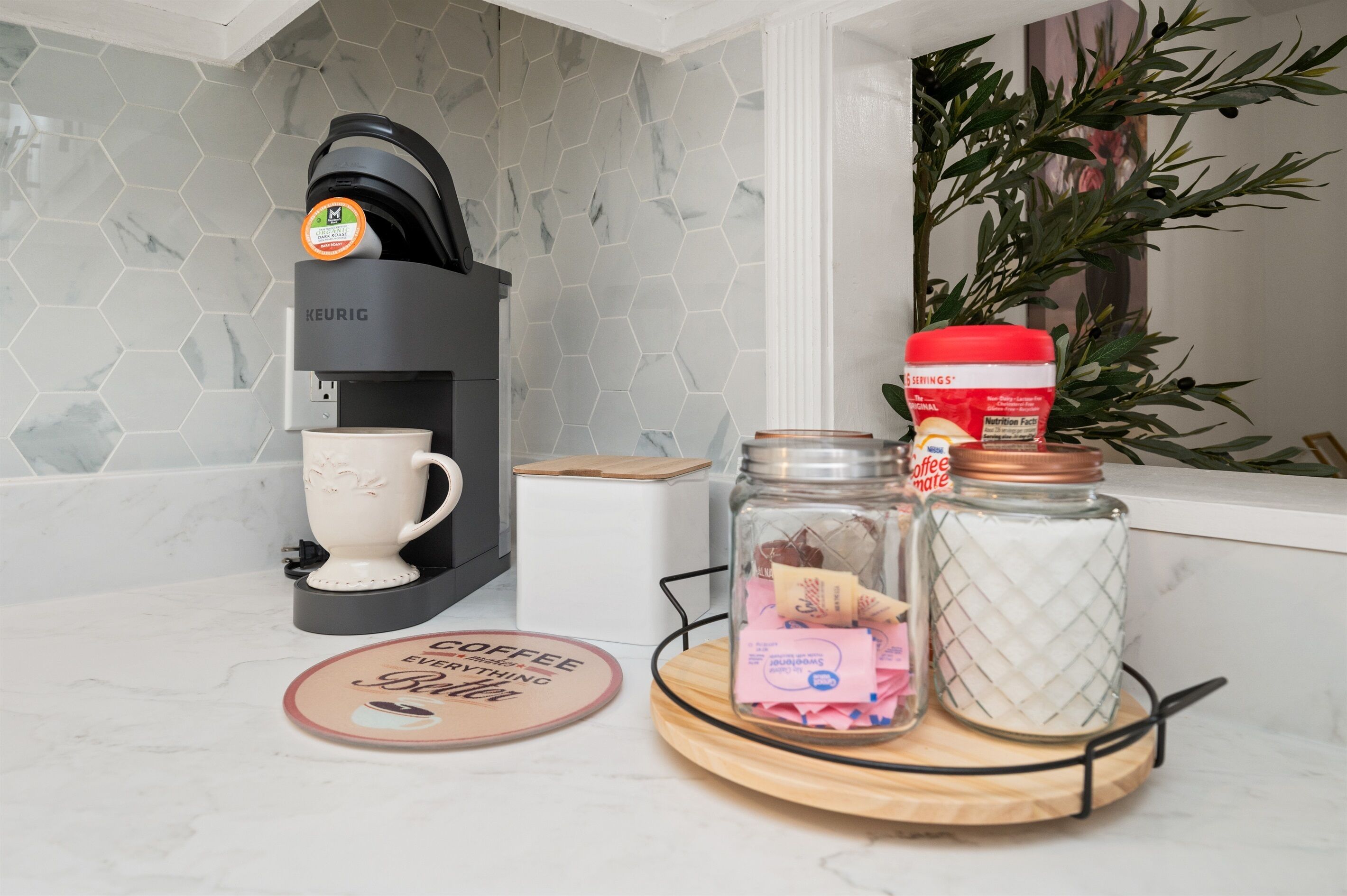Une machine à café, une tasse, un bocal contenant des dosettes de café et un plateau avec un dessous de verre sur le thème du café.