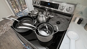 Una cocina con estufa de acero inoxidable, ollas, sartenes y un hervidor.