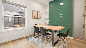 Zona pranzo moderna con tavolo in legno, sedie nere, parete verde decorativa e finestra con persiane.