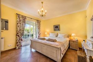 Une chambre à coucher avec un lit, deux lampes de chevet, un lustre, une fenêtre avec des rideaux et un tableau au mur.