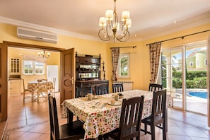 Un coin repas avec une table dressée pour quatre personnes, un lustre et une vue sur une piscine.