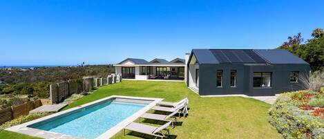 A modern house with a swimming pool, solar panels, and a view of the ocean.
