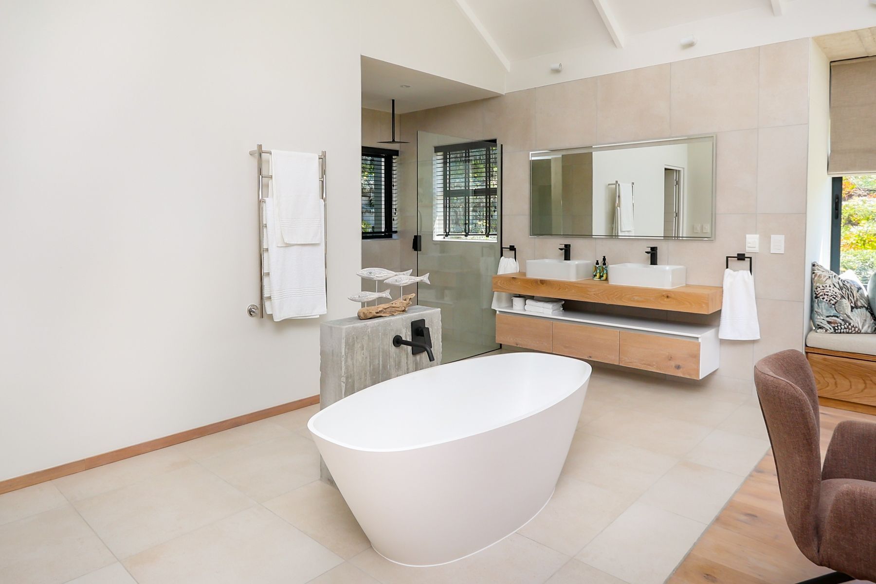 Un baño moderno con una bañera independiente, un tocador con espejo y una ventana con persianas.