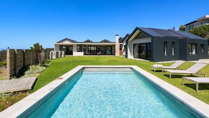 Una casa moderna con piscina, un porche cubierto y vista al océano.