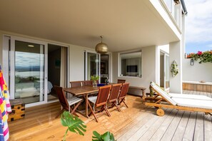 A wooden deck with a dining table and chairs, a lounge chair, and a large plant. - Busisiwe House - Four Bedroom Apartment, Sleeps 10 (Plettenberg Bay)