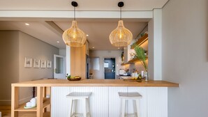 A modern kitchen with a central island, two barstools, pendant lighting, and a view into the adjacent dining area. - Busisiwe House - Four Bedroom Apartment, Sleeps 10 (Plettenberg Bay)