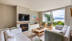 A modern living room with a fireplace, a flat-screen TV, and a view of the sea. - Busisiwe House - Four Bedroom Apartment, Sleeps 10 (Plettenberg Bay)