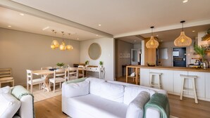A modern living room with a white sofa, dining area, and kitchen with bar stools. - Busisiwe House - Four Bedroom Apartment, Sleeps 10 (Plettenberg Bay)