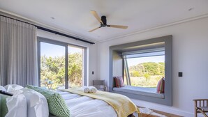 Une chambre à coucher avec un grand lit, un ventilateur de plafond et une fenêtre donnant sur un paysage verdoyant.
