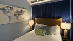 A neatly made bed with a world map on the wall, a headboard, two bedside lamps, and a blue curtain. - Lime Time (Coral Bay, St John)