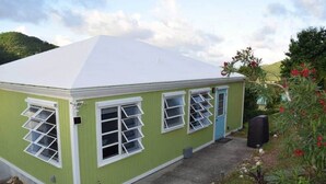 A small, single-story building with a white roof and green walls, featuring multiple windows and a door. - Lime Time (Coral Bay, St John)