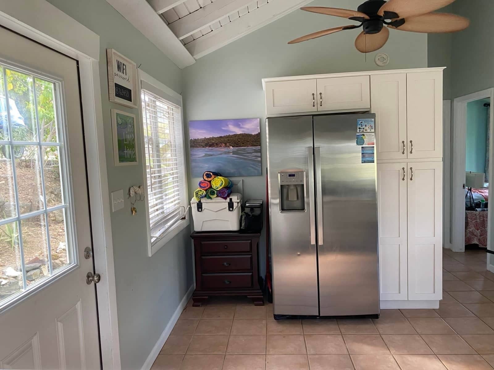 A kitchen with a stainless steel refrigerator, a water dispenser, and a window with blinds.