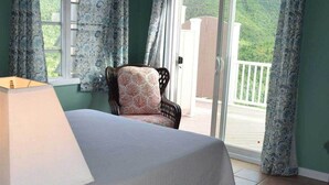 A bedroom with a bed, a chair, a lamp, and a view of a balcony. - Lime Time (Coral Bay, St John)