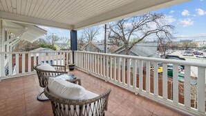 A covered balcony with wicker furniture and a view of a parking lot and houses. - The Abide on Magnolia (Fort Worth)
