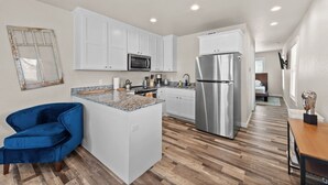 A modern kitchen with white cabinets, a stainless steel refrigerator, and a blue chair. - The Abide on Magnolia (Fort Worth)