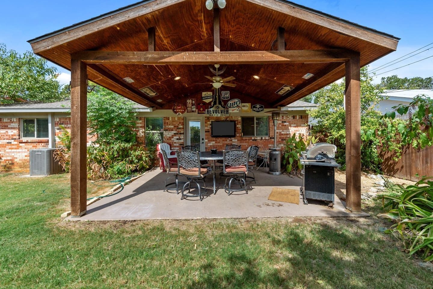 Eine überdachte Terrasse im Freien mit Backsteinwand, Grill und Gartenmöbeln.