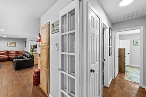 A hallway with a wooden floor, a brown leather couch, and a white door with a keypad lock. - Casa Tejas MidTerm Rental (Arlington)