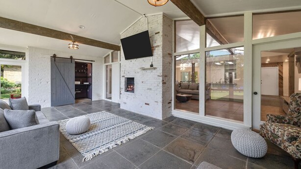 A spacious living area with a fireplace, large windows, and a sliding glass door leading to an outdoor space. - Its not Unusual MidTerm Rental (Arlington)