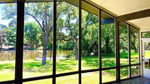 A room with large windows offering a view of a grassy yard and trees. - Its not Unusual MidTerm Rental (Arlington)