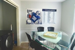 A dining area with a glass table, chairs, and a poster of a football player. - Terlingua MidTerm Rental (Arlington)