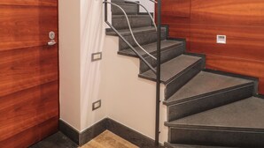 Una escalera con barandilla de metal, una puerta de madera y suelo de baldosas.