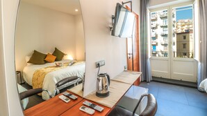 Una habitación de hotel con cama, escritorio con hervidor, televisión y vista a la ciudad por la ventana.