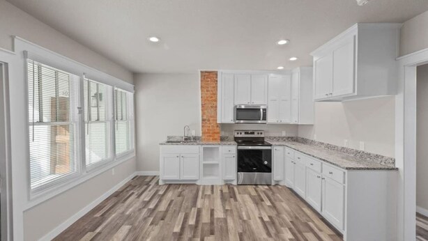 A modern kitchen with white cabinets, a brick accent wall, a built-in oven, and a microwave. - Thira on Magnolia Charming 1-bedroom house in nice Fort Worth with WiFi, AC (Fort Worth)