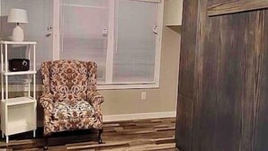 A room with a patterned armchair, a ceiling fan, and a wooden floor. - Thira on Magnolia Charming 1-bedroom house in nice Fort Worth with WiFi, AC (Fort Worth)