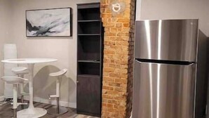 A modern kitchen with a stainless steel refrigerator, a stone accent wall, and a herringbone wood floor. - Thira on Magnolia Charming 1-bedroom house in nice Fort Worth with WiFi, AC (Fort Worth)